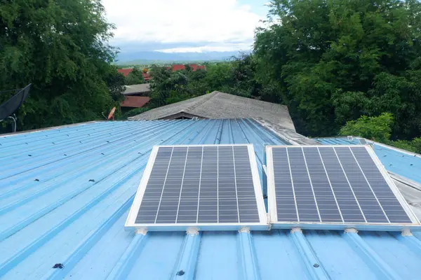 Kırsal bir evin mavi metal çatısına iki büyük güneş paneli monte edilir. Onları desteklemek için çelik bacaklar kullanılır..