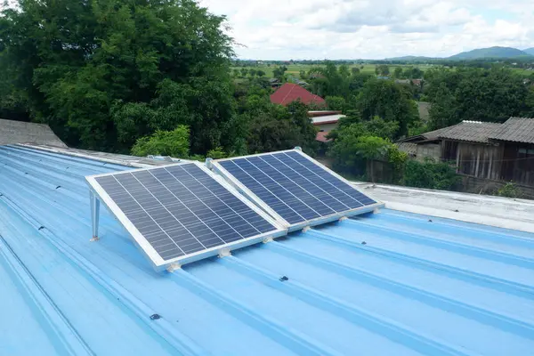 Kırsal bir evin mavi metal çatısına iki büyük güneş paneli monte edilir. Onları desteklemek için çelik bacaklar kullanılır..