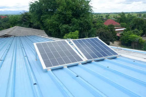 Kırsal bir evin mavi metal çatısına iki büyük güneş paneli monte edilir. Onları desteklemek için çelik bacaklar kullanılır..