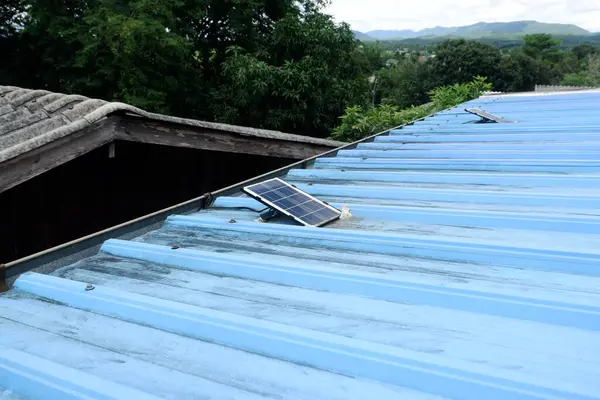Kırsal bir evin mavi metal çatısına kurulmuş küçük güneş panelleri.