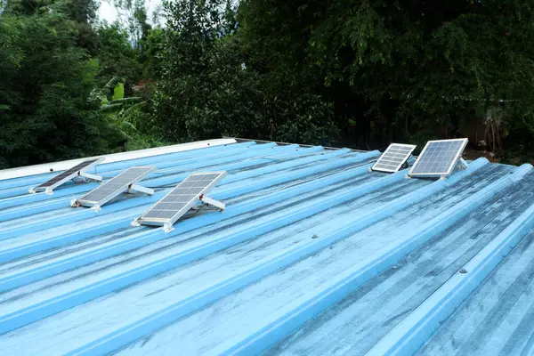 Kırsal bir evin mavi metal çatısına kurulmuş küçük güneş panelleri.