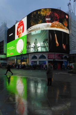 Piccadilly 'de ışıklı bir reklamla ıslak kaldırımda duran bir adam. Londra' nın merkezi.