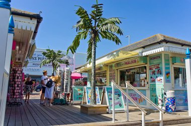 Skegness 'teki gezinti güvertesinde güneşli bir yaz gününde alışveriş yapan gençlerle dolu palmiye ağaçlarıyla kaplı Zevk Sahili.