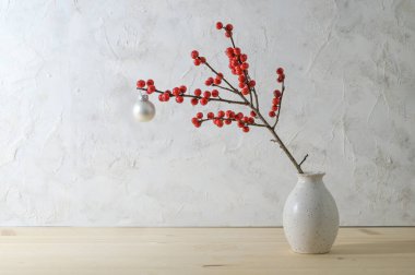 Kırmızı böğürtlenli Holly ya da ilex şubesi ve küçük bir vazoda beyaz bir noel topu alçılı bir duvara karşı, basit ama etkili bir kış süslemesi, kopyalama alanı