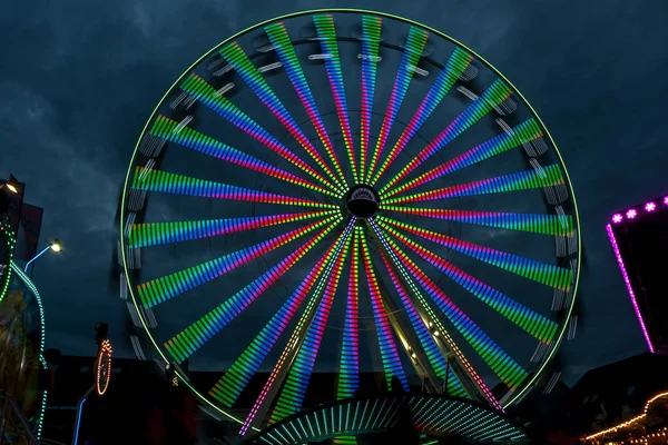 stock image Long exposure of a giant wheel in motion with colorful lights at a christmas fair against a cloudy night sky, abstract image, motion blur