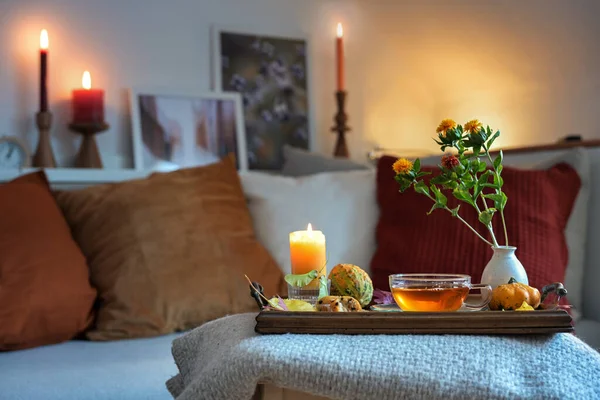 Relaxation with tea, candles and autumn decoration on a tablet in front of the couch in the cozy living room, copy space, selected focus, narrow depth of field