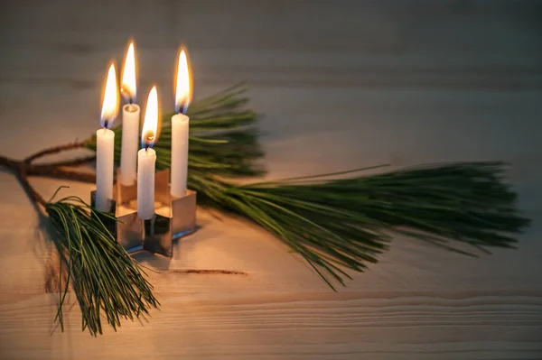 Four small advent candles placed on a cookie cutter in star shape and a pine branch on a wooden table, minimalist decoration in the Christmas season, copy space, selected focus, narrow depth of field