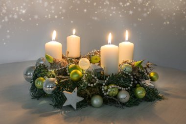 Fourth Advent, wreath with four burning white candles and green Christmas decoration on a table, home decor for the fourth Sunday, copy space, selected focus, narrow depth of field clipart