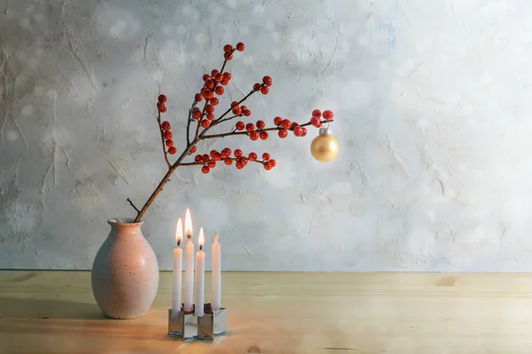 stock image Minimalist third advent with four small candles, three are burning and a berry branch with a golden christmas ball in a vase, snowy background with copy space, selected focus