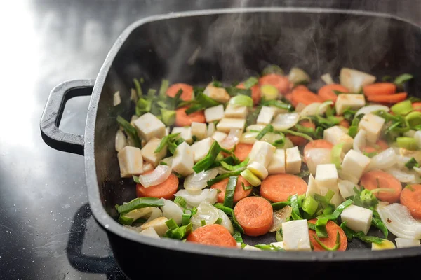 Steaming chopped vegetables in a black cooking pan, ingredients for soups or sauces with carrots, onions, leeks and celery, copy space, selected focus, narrow depth of field