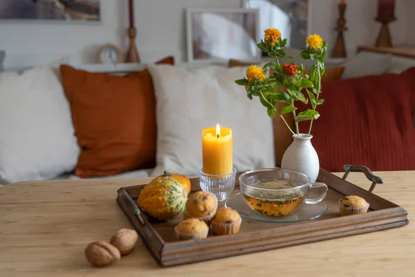 Tray with a cup of tea, lit candle and autumn decoration on a table in the living room, cozy home in the cold season, copy space, selected focus, narrow depth of field