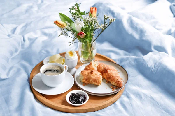 Happy morning with breakfast in bed, flowers, croissant, coffee and more on a tray on blue white linen at birthday, valentines or mothers day, copy space, selected soft focus, narrow depth of field