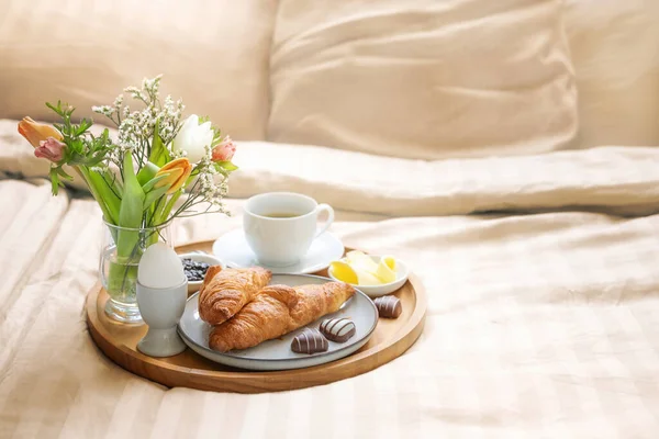 Romantic breakfast in bed with flowers, croissant, coffee cup and hearts from chocolate on beige bed linen for valentines  or mothers day, copy space, selected soft focus, narrow depth of field