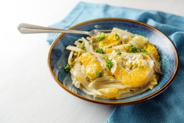 Dish of chicory and orange with spring onions on a blue plate and napkin on a white wooden table, healthy vegetarian meal for a low carb diet, copy space, selected focus, narrow depth of field