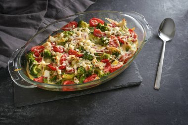 Vegetable casserole with broccoli, tomatoes, onions and feta cheese in a glass baking dish on a dark gray slate surface, copy space, selected focus, narrow depth of field