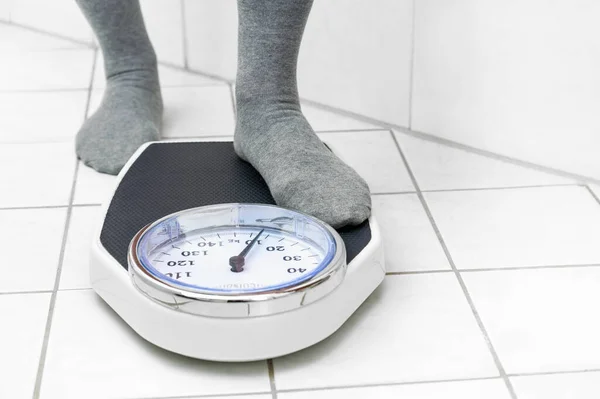 Feet in socks stepping on a personal scale on the tiled bathroom floor to measure the body weight, copy space, selected focus
