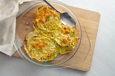Gratinated slices of Chinese or napa cabbage in a glass casserole on a wooden kitchen board, creative vegetarian dish, high angle view from above, copy space, selected focus