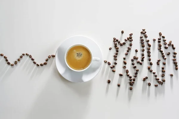 Coffee beans in a calm curve lead to a coffee cup, afterwards the beans show an exited messy pattern, concept for over stimulating effect on heart rhythm of caffeine, high angle view, copy space