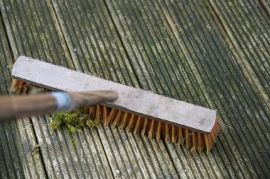 Yosun ve yosunları temizlemek için yıpranmış ahşap bir güverteyi ovalayan plastik tüylü dış süpürge, bahçede ve bahçede bahar temizliği, kopyalama alanı, seçilmiş odak alanı, dar alan derinliği