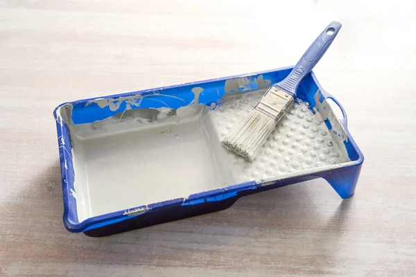 Blue paint tray with light gray lacquer and a brush on a wooden table, craft concept for renovation, painting and do it yourself, copy space, selected focus