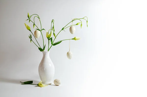 明るい灰色の背景にイースターエッグをぶら下げて飾られた白い花瓶の繊細な花の束 コピースペース 選択された焦点 フィールドの狭い深さ — ストック写真