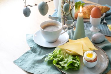 Ekmek rulosu, peynir, kaynamış yumurta ve kahve ile kahvaltı masası pastel turkuaz peçete, süs olarak paskalya yumurtası ve mumu asmak, kopya alanı, seçilmiş odak alanı, dar alan derinliği