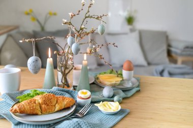 Küçük bir oturma odasında haşlanmış yumurta, kruvasan ve pastel turkuaz paskalya süslemesi, fotokopi masası, seçilmiş odak, dar alan derinliği.