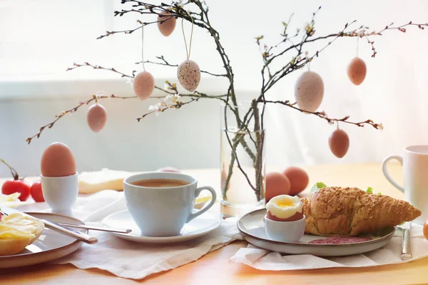 复活节早餐在早晨的阳光下 桌上放着咖啡和羊角面包 春枝上挂着天然鸡蛋装饰 复制空间 选择了柔和的焦点 狭窄的田野深度 — 图库照片