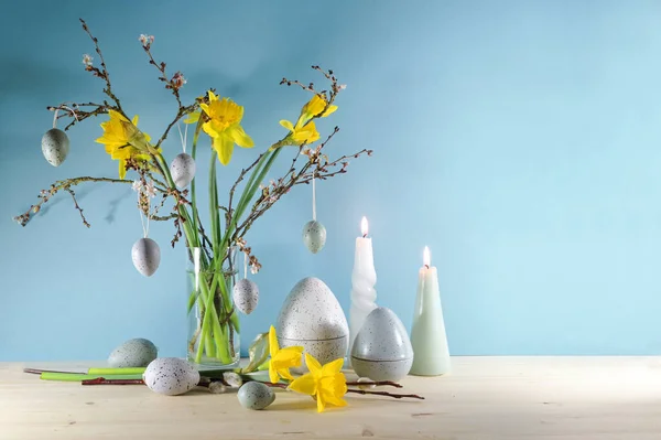キャンドル ガラスの花瓶と人工灰色のイースターエッグの春の枝の花束と季節の休日の装飾青い壁 コピースペース フォーカスを選択した木製のボード上の — ストック写真
