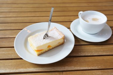 Mandalinalı bir parça cheesecake, krema şekeri, bir pasta çatalı ve kafedeki ahşap masada bir fincan kahve, kopyalama alanı, seçilmiş odak, dar alan derinliği.