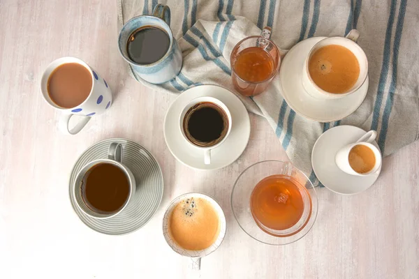 几个不同的杯子和杯子 茶杯上有咖啡和茶水 放在一张浅色的桌子上 上面有一条蓝色的灰色毛巾 从上面可以看到很高的角度 选择的焦点 狭窄的田野深度 — 图库照片