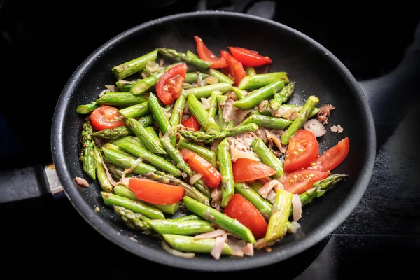 ストーブの上に黒いフライパンで緑のアスパラガス トマト パルマハム 健康的な春の食事を調理し 焦点を選択し フィールドの狭い深さ — ストック写真