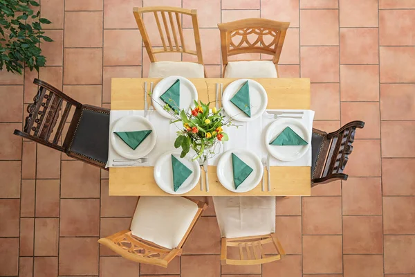 白いプレート カトラリー 緑のナプキンと花の花束 タイル張りのテラコッタの床に異なるヴィンテージの椅子 上からの高い角度ビュー 選択されたフォーカスを持つ6のための場所の設定を持つ木製のテーブル — ストック写真