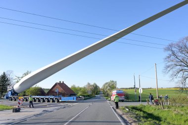 Heavy duty transport of a windmill blade lifted up to avoid obstacles such as a power lines on a narrow country road junction, industry for renewable energy, blue sky, copy space, selected focus clipart