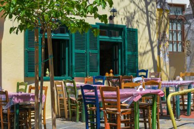 Yunanistan 'ın Selanik kentindeki geleneksel bir evin pencerelerinin önündeki masalarda farklı boyalı ahşap sandalyeli sıradan sokak restoranı veya Rustik Akdeniz tavernası