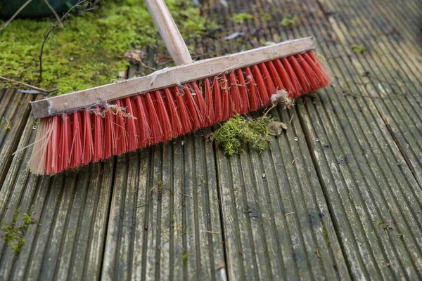 滑りやすい藻類や苔と風化した木製のデッキに赤いプラスチック製の毛を持つ屋外のほうき 庭や庭で春のクリーニング コピースペース 選択されたフォーカス フィールドの狭い深さ — ストック写真
