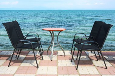 Siyah açık hava sandalyeleri ve doğrudan mavi Akdeniz kıyısında asfalt bir bistro masası, yaz tatilinde turistler için bir kaldırım kafesi kurulumu, fotokopi alanı