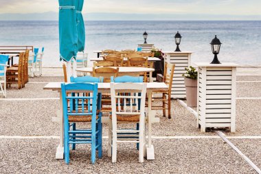 Denizin yanındaki terasta bulunan bir tavernada mavi ve beyaz ahşap sandalye ve masalar, Yunanistan 'ın Chalkidiki kentindeki turizm merkezi, seçilmiş odak noktası