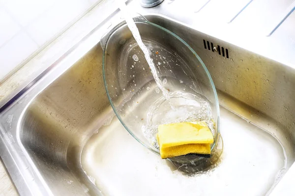 シンク内のガラス鍋は 水の流れの下で黄色のスポンジと食器洗浄洗剤で洗浄され 迷惑な家事のコア コピースペース 選択されたソフトフォーカス — ストック写真