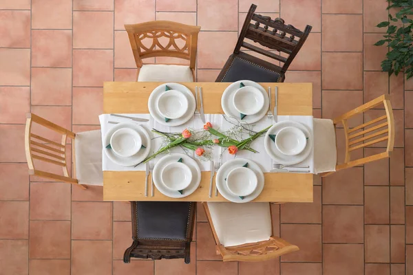 6つの空の白いプレートとボウル カトラリー いくつかのチューリップの花 タイル張りのテラコッタの床の周りの異なるヴィンテージの椅子 上からの高い角度のビュー 選択されたフォーカスを持つ木製のテーブル設定 — ストック写真