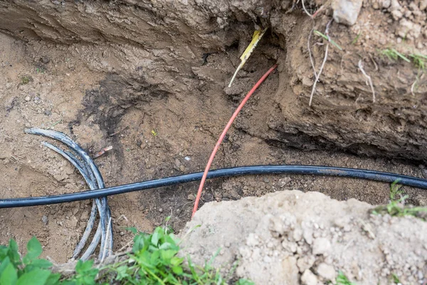 不同的电线和光纤电缆混杂在房子附近的地面上 挖掘新装置时的危险 复制空间 选定的焦点 — 图库照片