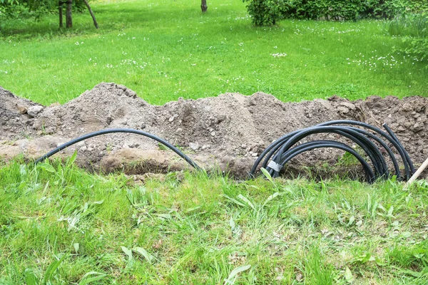 在花园对面的草坪上 黑色的电力电缆被放置在一个狭窄的沟槽里 因为它比头顶的电线 复制空间 选定的焦距更安全 — 图库照片