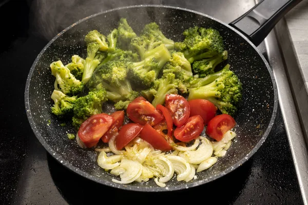 玉ねぎ トマト ブロッコリーは 健康的な菜食主義者の食事 選択された焦点 フィールドの狭い深さのための黒いストーブの上に蒸しフライパンでソテーされています — ストック写真