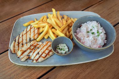 Kızarmış tavuk filetosu, patates kızartması, tereyağı ve lahana salatası, ahşap bir masada mavi tabaklarda servis ediliyor, lezzetli ama sağlıksız fast food, seçilmiş odak, dar tarla derinliği