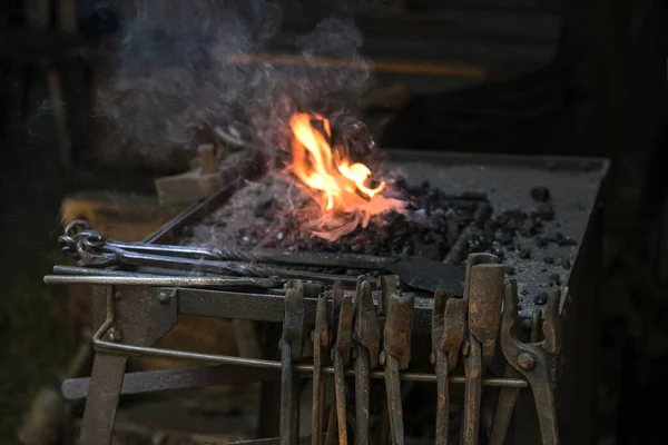 stock image Portable forge of a blacksmith with various rusty tongs and a flaming coal fire at a historic craft market, copy space, selected focus, narrow depth of field