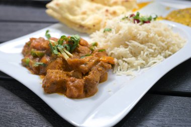 Hint yemeği, baharatlı soslu biftek, beyaz tabakta pirinç ve ekmek ve siyah masa, seçilmiş odak, dar alan derinliği