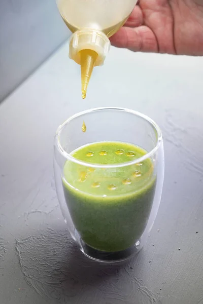 Flavored Oil Druppelend Uit Een Fles Een Glas Groene Spinazie — Stockfoto