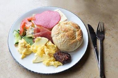 Ekmek dilimli kahvaltı tabağı, çırpılmış yumurta, sosis, peynir ve tereyağlı çatal bıçak takımı, seçilmiş odak noktası, dar alan derinliği.