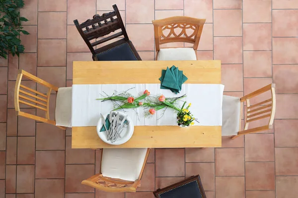 准备一张桌子 桌上有白色的盘子和碗 绿色的餐巾和一些郁金香花 不同的木制椅子围绕在瓷砖地板上 从上方的高角度看 选择焦点 — 图库照片