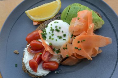 Kahvaltı, brunch ya da öğle yemeği sandviçi kızarmış çavdar ekmeği, krem peynir, domates, haşlanmış yumurta, avokado ve ince dilimlenmiş havuç mavi tabakta, üst manzara, seçilmiş alan derinliği